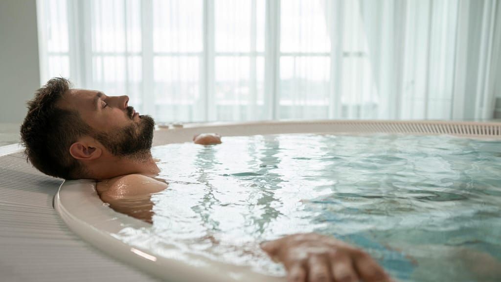 Hidroterapia en frío para el metabolismo Hombre sumergido en una tina de agua fría practicando cold plunge para activar la grasa parda supraclavicular.