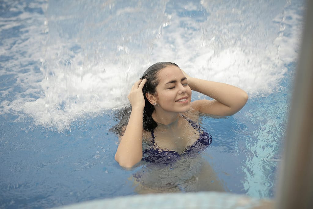 Beneficios del agua fría: La ciencia detrás del "Cold Plunge". Mujer disfrutando de hidroterapia bajo una cascada de agua fría.