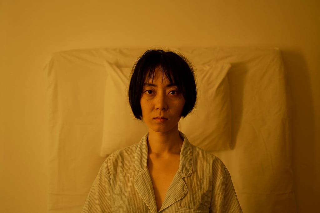 insomnio-hidroterapia. Mujer sentada en la cama con expresión de agotamiento por insomnio, iluminación cálida de noche.
