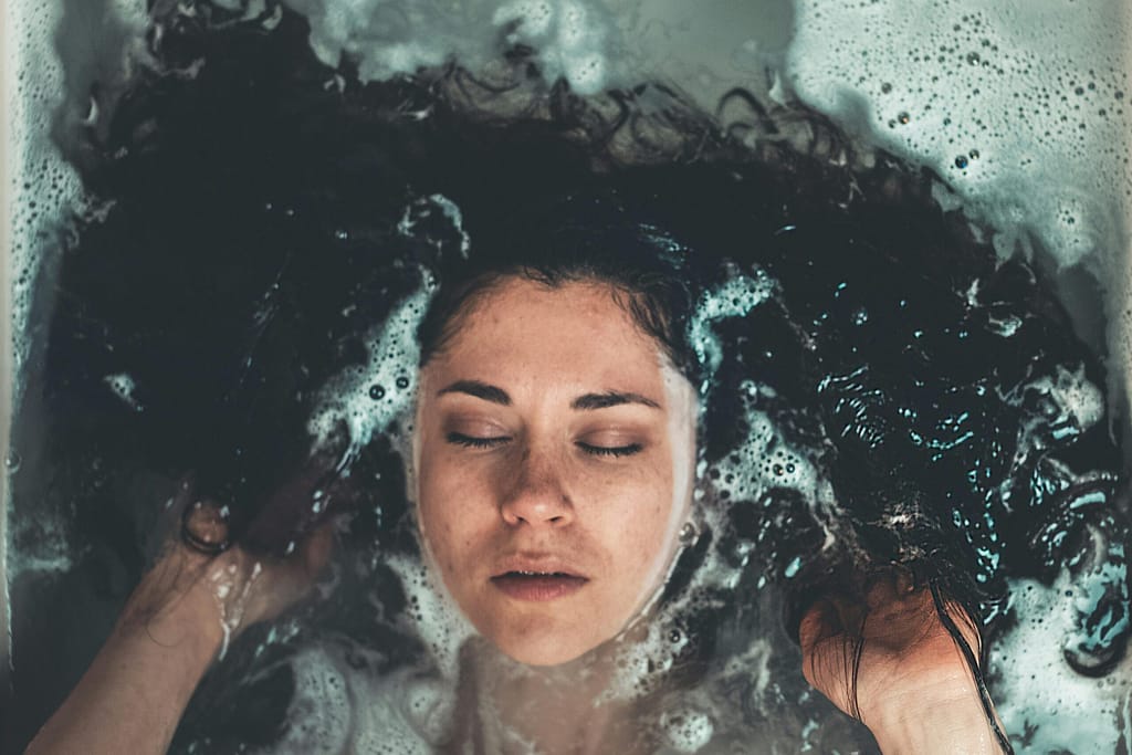 Beneficios del agua fría: La ciencia detrás del "Cold Plunge". Primer plano de rostro de mujer sumergido en agua fría con burbujas y cabello expandido.