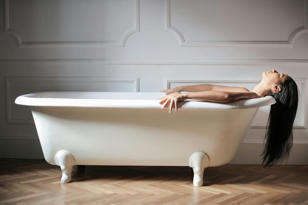 Ducha-Hidroterapia-Metodo-Kneipp Mujer relajada en una bañera blanca practicando hidroterapia de contraste térmico en casa.