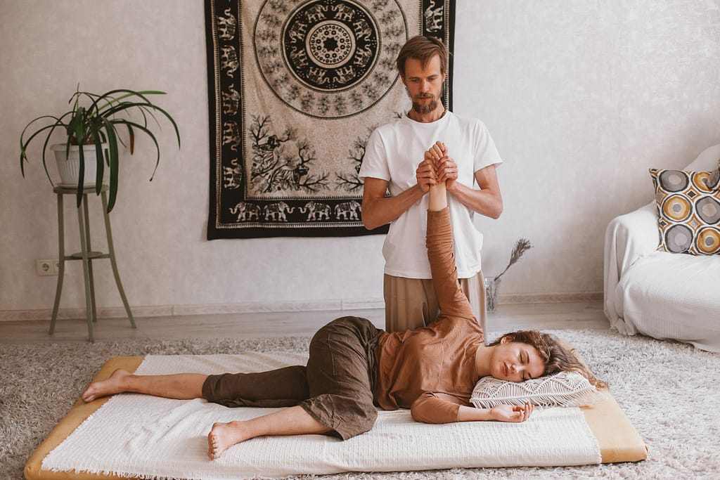 shiatsu-terapia-holistica-origenes Terapeuta aplicando un estiramiento de Shiatsu japonés en un futón, mostrando las bases de la acupresión y la terapia holística corporal.