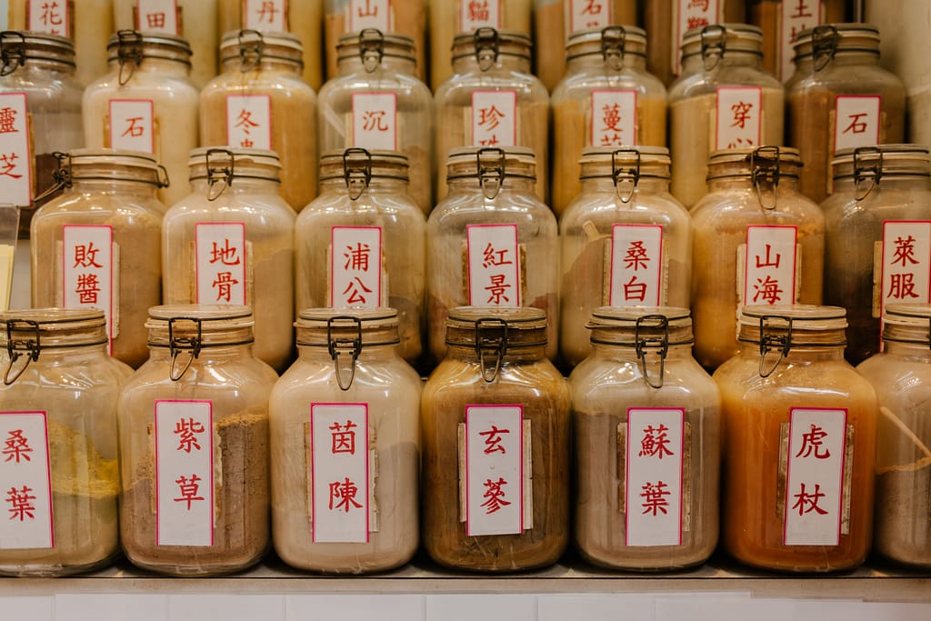 extractos-herbales-medicina-tradicional-china Frascos de vidrio alineados con extractos de plantas y hierbas medicinales chinas etiquetadas con caracteres tradicionales para terapias de bienestar.