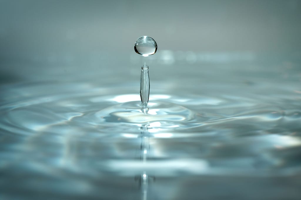 principios-biofisicos-y-quimicos-del-agua Una gota de agua suspendida en el aire creando ondas concéntricas en la superficie, representando los principios físicos y de termodinamica del agua.