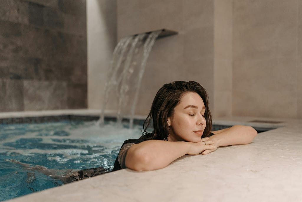 burnout e hidroterapia Mujer relajada en una piscina de hidroterapia con caída de agua, experimentando alivio del estrés y burnout mediante inmersión terapéutica.