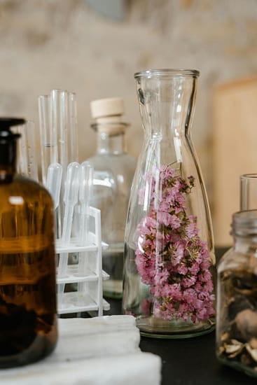 Frascos de laboratorio con flores. Frascos de vidrio de laboratorio con flores rosadas en su interior junto a pipetas y envases de boticario sobre una mesa para la elaboración de terapias naturales.