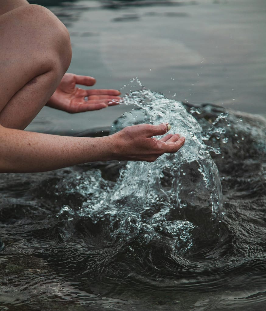 Hidroterapia: 4 técnicas para regular la ansiedad y depresión. Manos humanas interactuando con agua natural en movimiento, representando la conexión biológica y la hidroterapia para el bienestar mental.